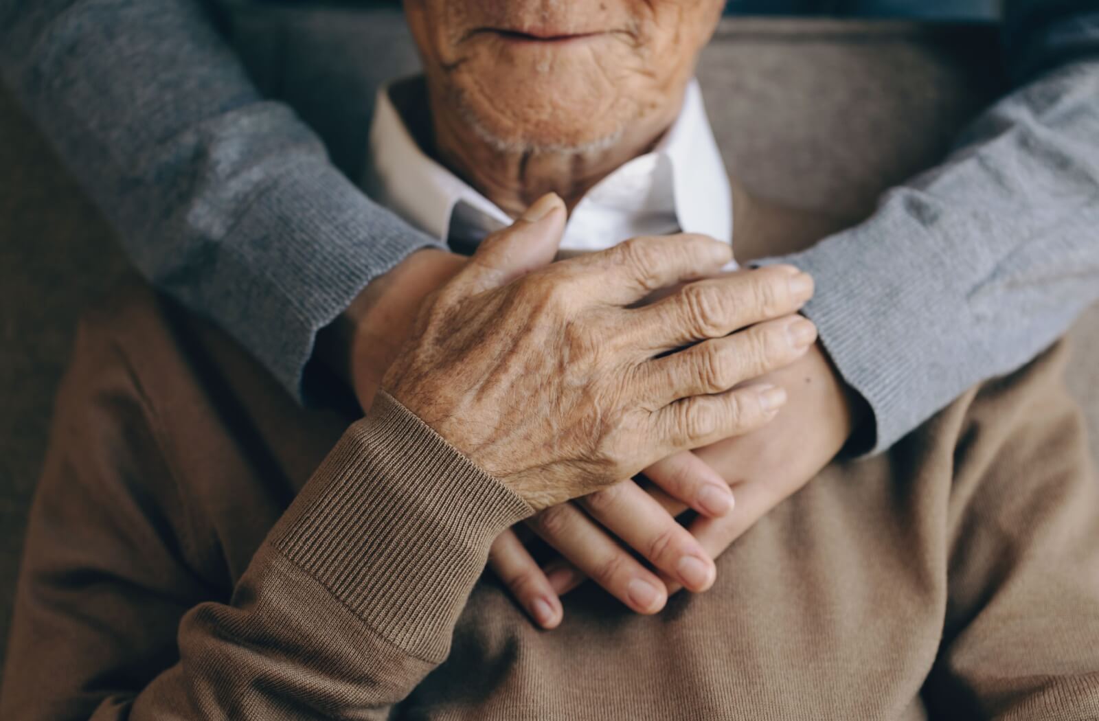 A close-up of a senior with their loved one's arms around them.