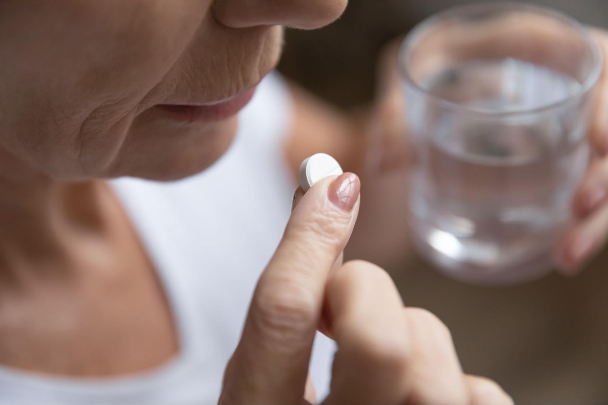 Close-up of an older adult holding a glass of water in their left hand and medication in their right hand.