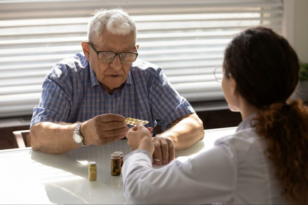 A female healthcare professional and an older adult sitting at a table looking at and discussing medication.