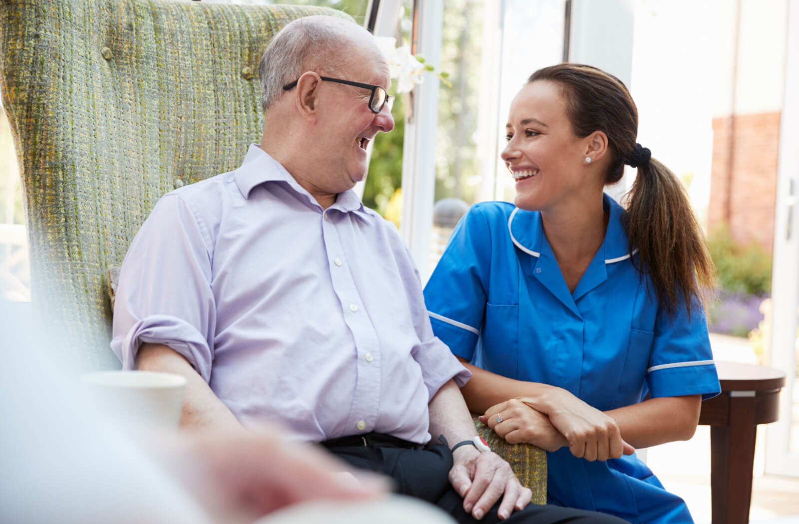 A happy older adult man in memory care sitting with a smiling nurse.