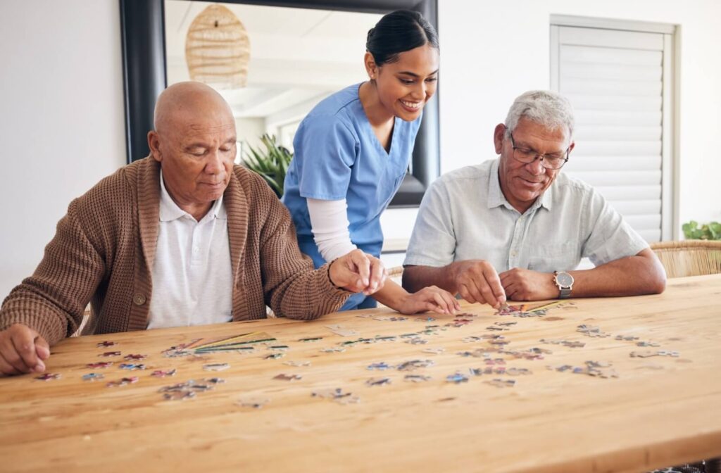 Two seniors and a caregiver complete a jigsaw puzzle together.