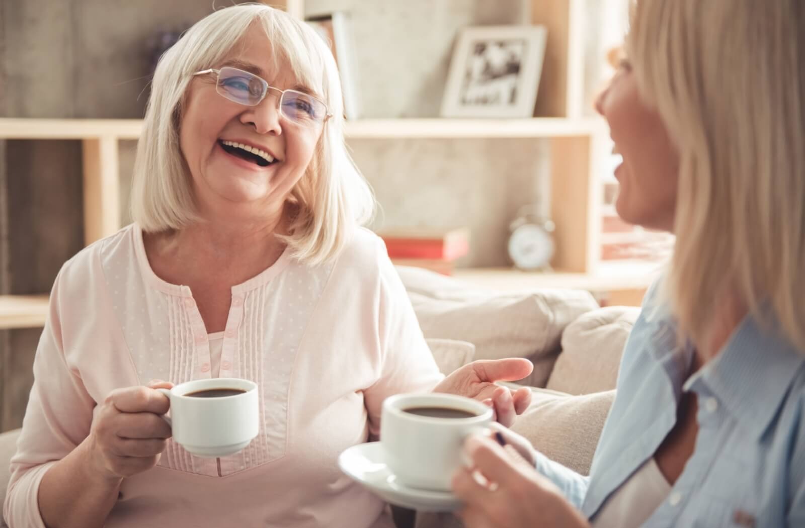 two seniors laugh and drink coffee